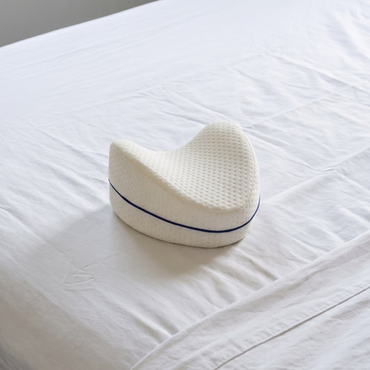 Cojín Alinea sobre una cama con sábanas blancas: forma de gota maciza, cara superior cóncava, funda blanca de jacquard con vivo azul marino.